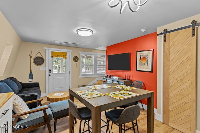 dining space featuring a barn door, baseboards, visible vents, and light wood-type flooring