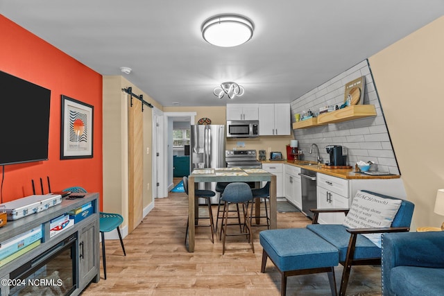 kitchen featuring appliances with stainless steel finishes, sink, white cabinets, a barn door, and light wood-type flooring