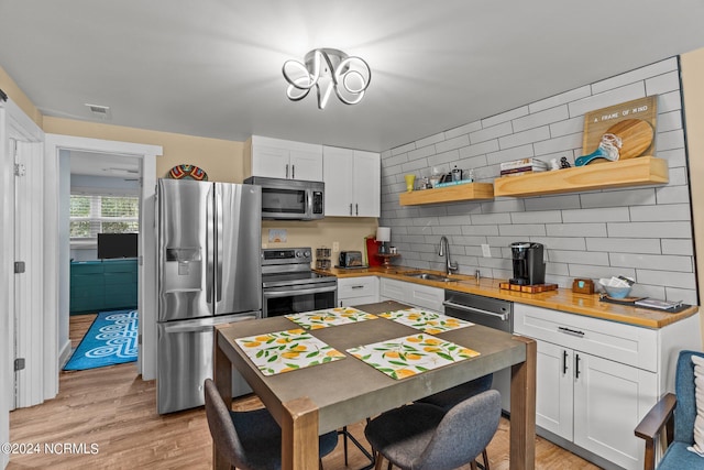 kitchen featuring white cabinets, stainless steel appliances, open shelves, backsplash, and a sink