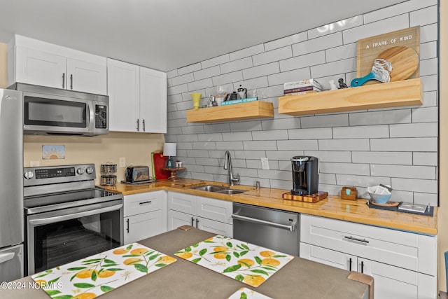 kitchen with butcher block countertops, white cabinetry, sink, backsplash, and stainless steel appliances