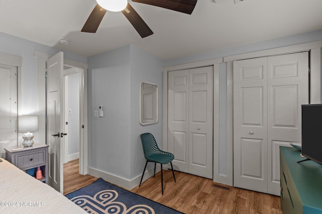 bedroom featuring baseboards, wood finished floors, two closets, and ceiling fan