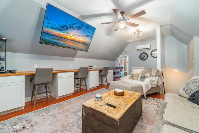 bedroom with ceiling fan, light hardwood / wood-style floors, a wall mounted AC, built in desk, and vaulted ceiling