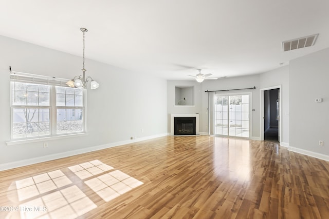 unfurnished living room with ceiling fan with notable chandelier and light hardwood / wood-style flooring