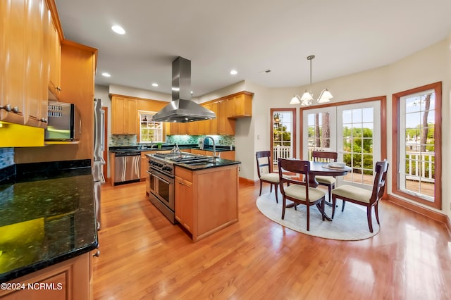 kitchen featuring hanging light fixtures, island range hood, a center island with sink, light hardwood / wood-style flooring, and appliances with stainless steel finishes