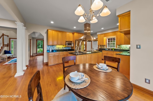 dining space with ornate columns, an inviting chandelier, sink, and light hardwood / wood-style floors