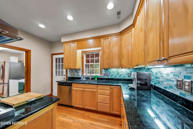 kitchen featuring decorative backsplash, light wood-type flooring, dark stone countertops, sink, and stainless steel appliances