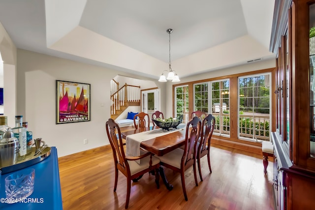 dining space featuring an inviting chandelier, hardwood / wood-style flooring, and a tray ceiling