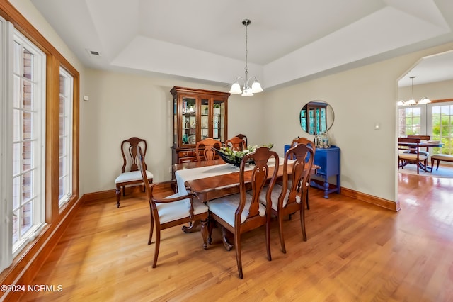 dining space featuring a notable chandelier, light hardwood / wood-style flooring, and a tray ceiling