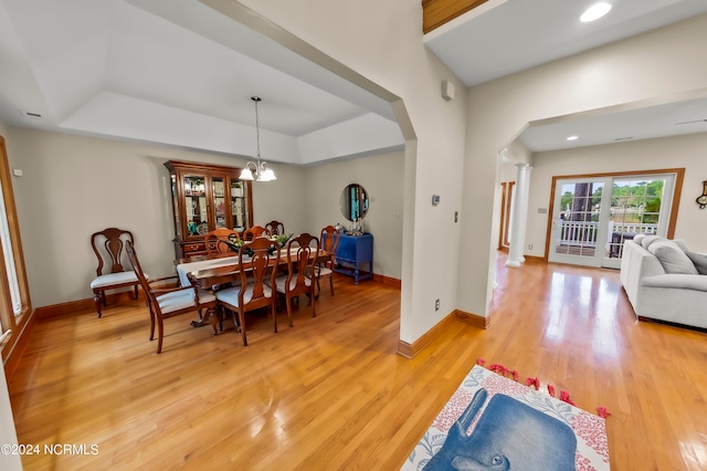 dining room with wood-type flooring, an inviting chandelier, a tray ceiling, and ornate columns