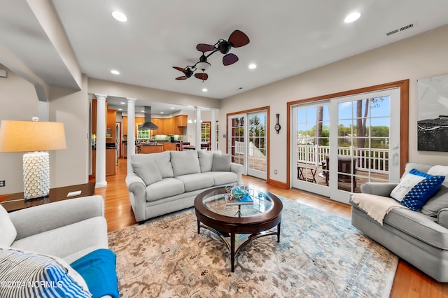 living room with decorative columns, light hardwood / wood-style flooring, and ceiling fan