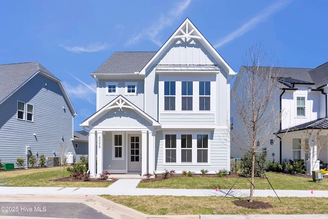 view of front facade with a shingled roof, a front yard, and board and batten siding