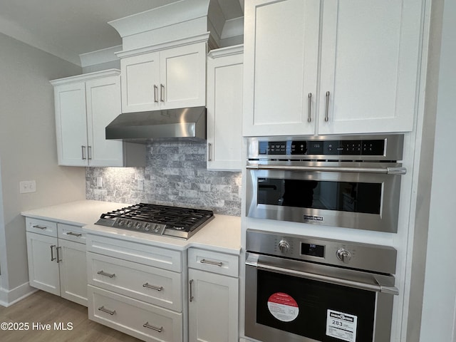 kitchen with stainless steel appliances, light countertops, decorative backsplash, white cabinets, and under cabinet range hood