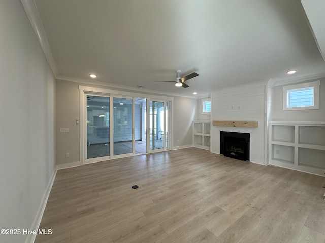 unfurnished living room featuring crown molding, a large fireplace, ceiling fan, wood finished floors, and baseboards