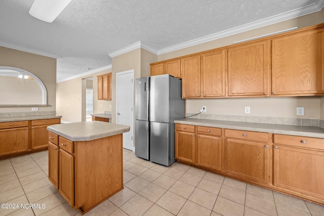 kitchen with stainless steel refrigerator, crown molding, a kitchen island, light tile patterned floors, and a textured ceiling