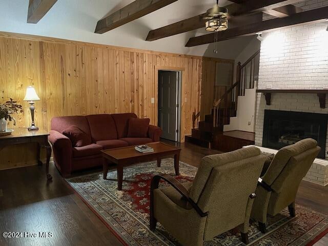 living room featuring wood walls, dark wood-type flooring, vaulted ceiling with beams, ceiling fan, and a fireplace