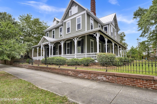 view of front facade with a standing seam roof, a porch, a chimney, metal roof, and fence