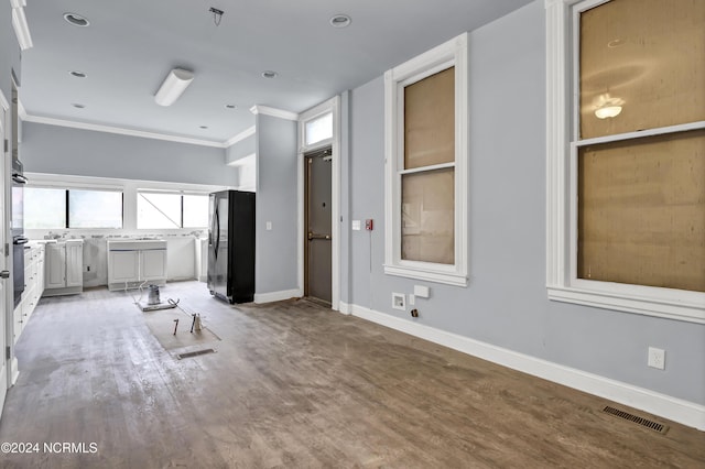 unfurnished living room featuring light wood-style flooring, visible vents, a wealth of natural light, and ornamental molding