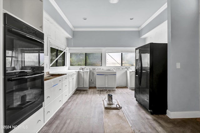 kitchen featuring light wood-type flooring, light countertops, black appliances, and crown molding