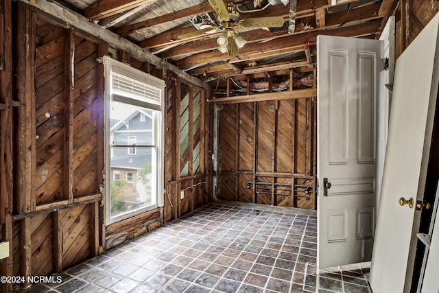 miscellaneous room featuring plenty of natural light, a ceiling fan, wood walls, and stone finish flooring