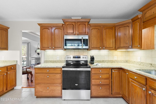 kitchen with light stone counters, light tile patterned flooring, ornamental molding, appliances with stainless steel finishes, and decorative backsplash