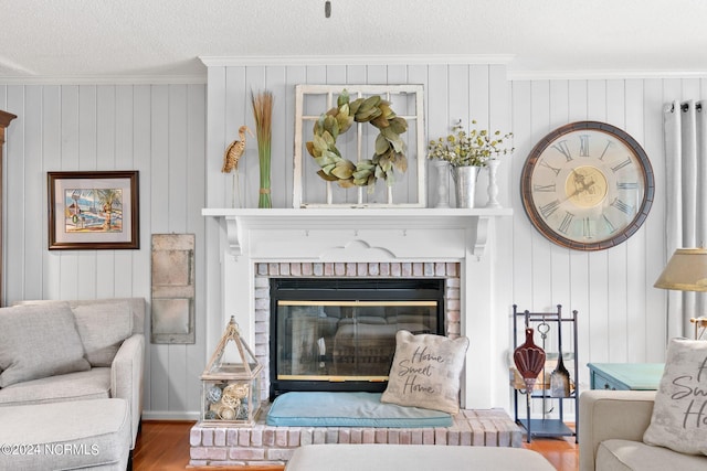 living room featuring wood walls, a brick fireplace, crown molding, hardwood / wood-style floors, and a textured ceiling