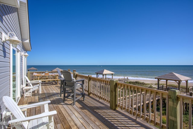 wooden deck with a water view, a gazebo, and a view of the beach