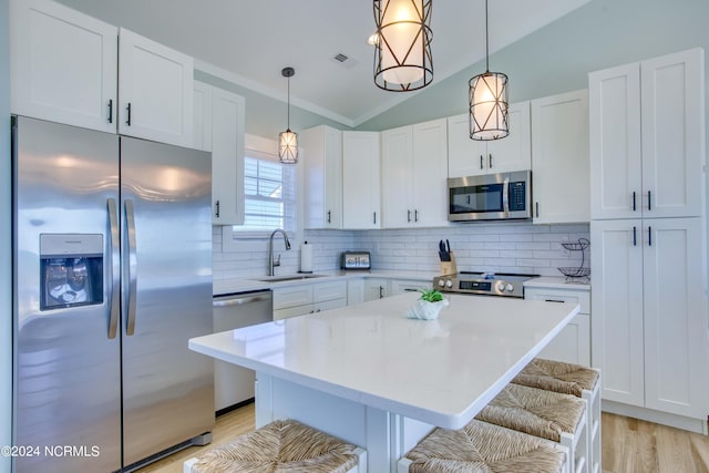 kitchen featuring a breakfast bar area, sink, stainless steel appliances, hanging light fixtures, and white cabinets