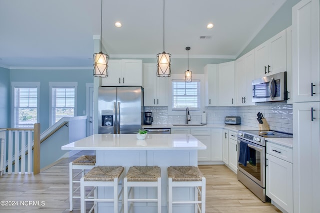 kitchen with sink, a kitchen island, white cabinetry, appliances with stainless steel finishes, and a breakfast bar area