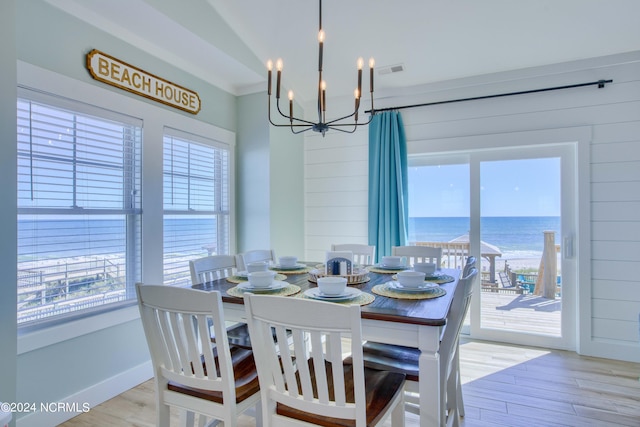 dining room with a water view, wooden walls, light hardwood / wood-style flooring, and a wealth of natural light