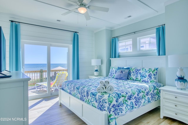 bedroom featuring access to outside, ceiling fan, wooden walls, light hardwood / wood-style floors, and a water view