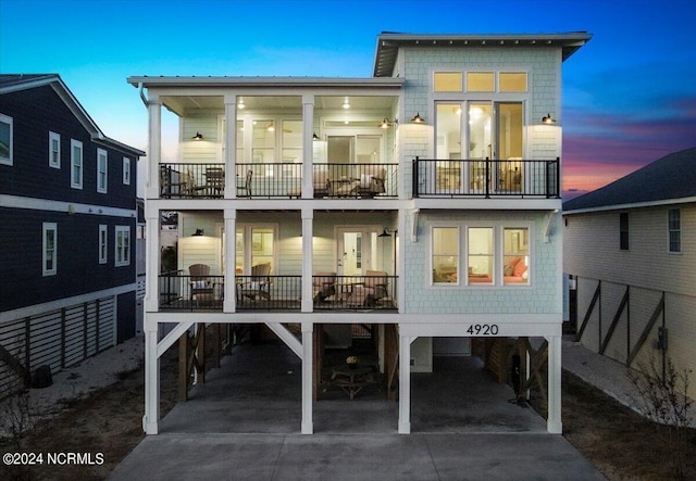 back house at dusk with a balcony and a carport