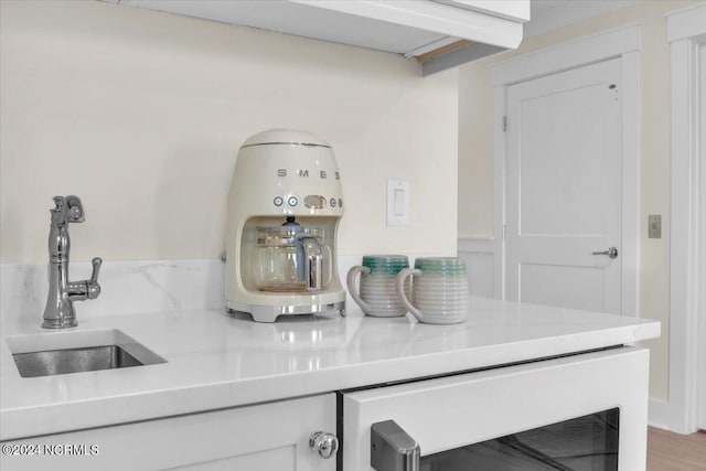 bar featuring white cabinets, wood-type flooring, light stone countertops, sink, and beverage cooler