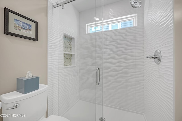 bathroom featuring a shower with door and toilet