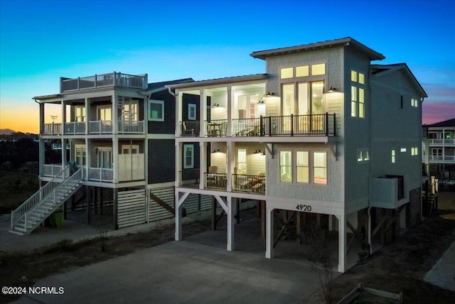 back house at dusk featuring a carport and a balcony