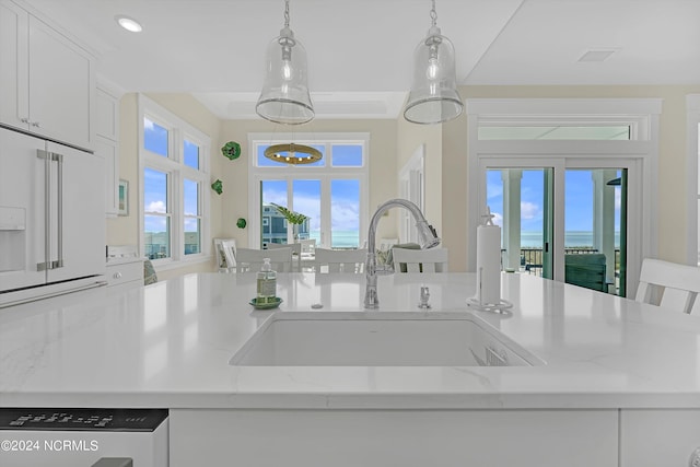 kitchen featuring high end white fridge, sink, decorative light fixtures, white cabinetry, and light stone counters