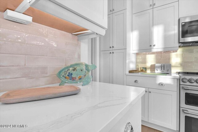 kitchen with tasteful backsplash, light stone countertops, white range with electric cooktop, and white cabinets