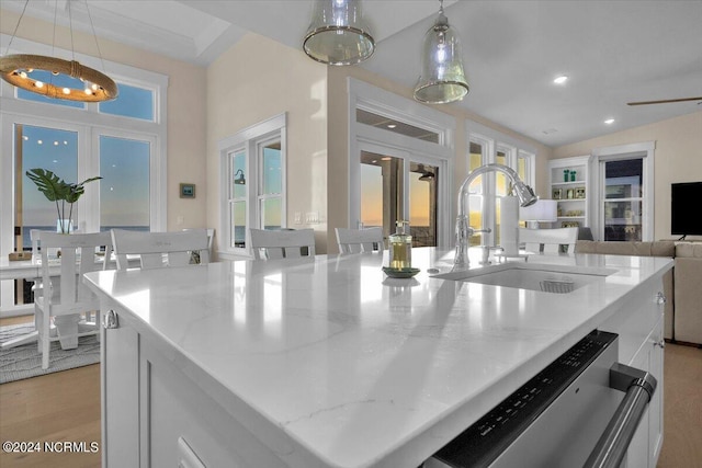 kitchen with stainless steel dishwasher, sink, a kitchen island with sink, and hanging light fixtures