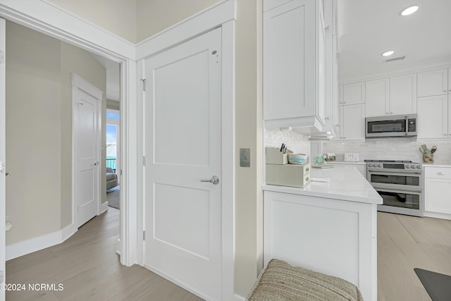 kitchen featuring backsplash, appliances with stainless steel finishes, light wood-type flooring, and white cabinets