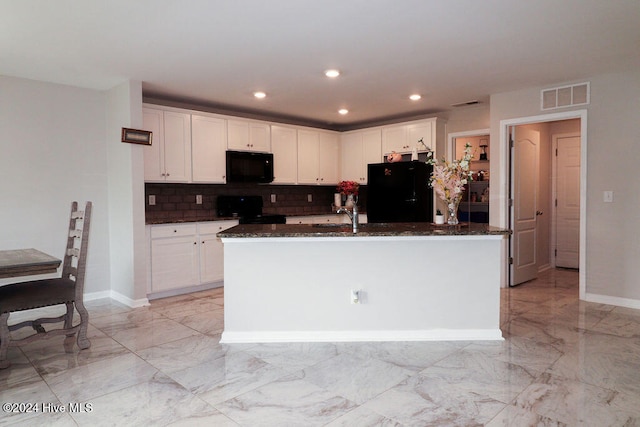 kitchen featuring white cabinets, black appliances, a center island with sink, and dark stone counters