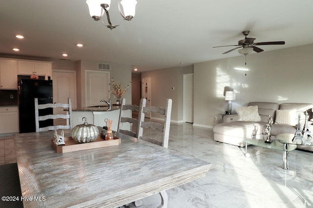 kitchen featuring white cabinetry, sink, black refrigerator, and ceiling fan with notable chandelier