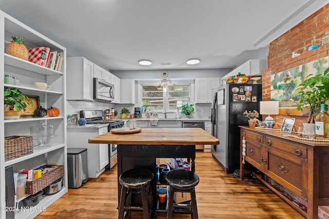 kitchen with white cabinets, a kitchen bar, stainless steel appliances, and light hardwood / wood-style flooring