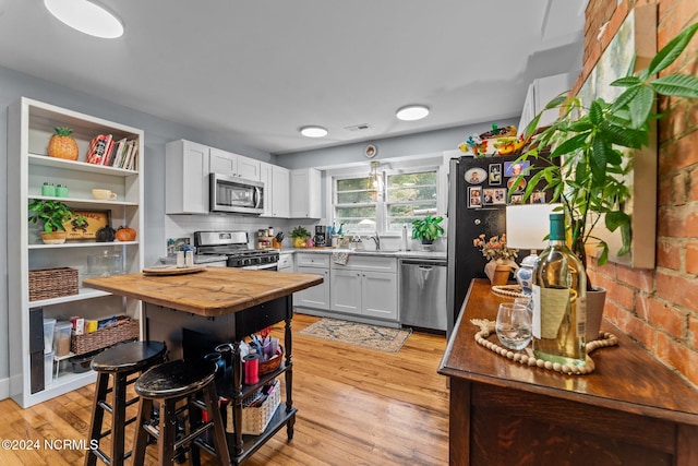 kitchen with stainless steel appliances, white cabinetry, wood counters, a breakfast bar area, and light hardwood / wood-style flooring