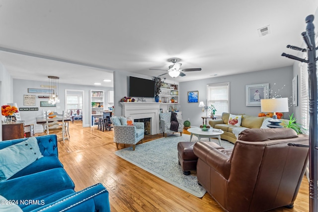 living room with ceiling fan with notable chandelier and light hardwood / wood-style floors