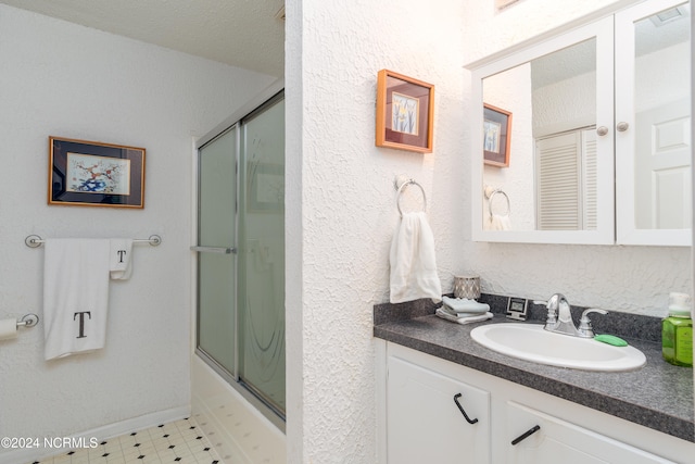 bathroom with shower / bath combination with glass door, vanity, and a textured ceiling