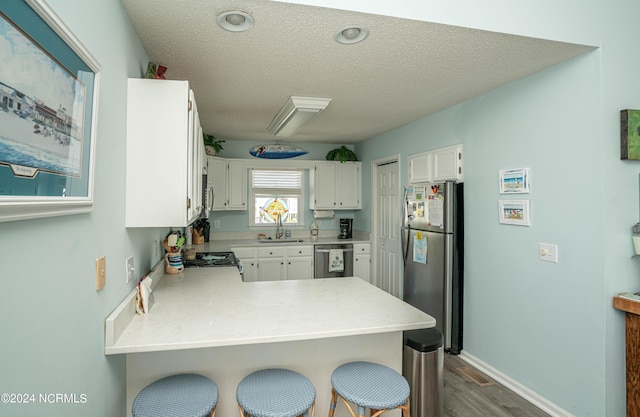 kitchen with kitchen peninsula, stainless steel appliances, sink, white cabinetry, and dark hardwood / wood-style flooring