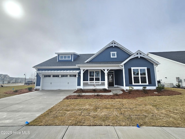 view of front facade featuring roof with shingles, a porch, an attached garage, driveway, and a front lawn