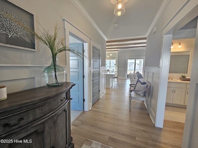 corridor featuring a decorative wall, light wood-type flooring, a sink, and crown molding