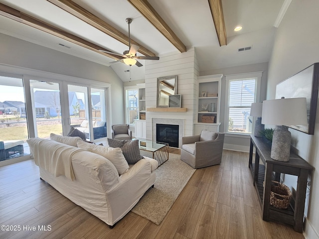 living room featuring a glass covered fireplace, visible vents, lofted ceiling with beams, and wood finished floors