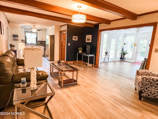 living room featuring beamed ceiling, light wood-type flooring, crown molding, and a healthy amount of sunlight