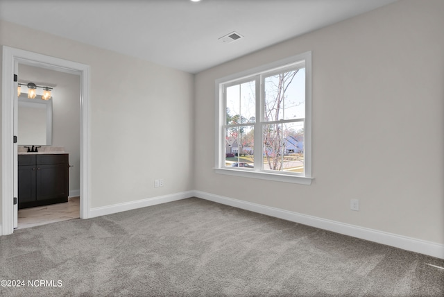 unfurnished bedroom with visible vents, light colored carpet, ensuite bathroom, and baseboards